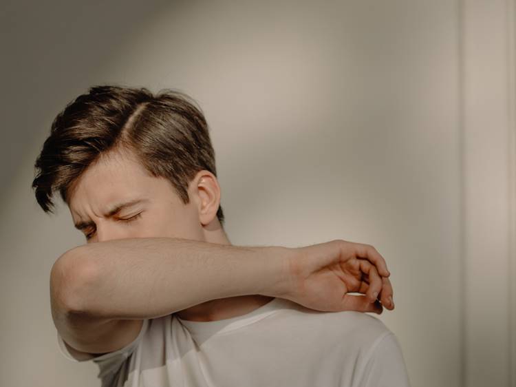 Man in white t-shirt coughing into elbow