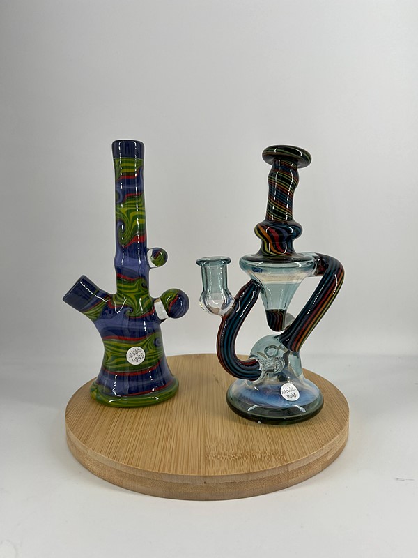 Two multicolored heady glass bongs on wooden circular display stand
