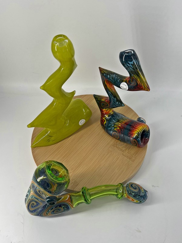 Two zig-zag shaped heady glass pipes on wooden circular stand and adjacent multicolored pipe